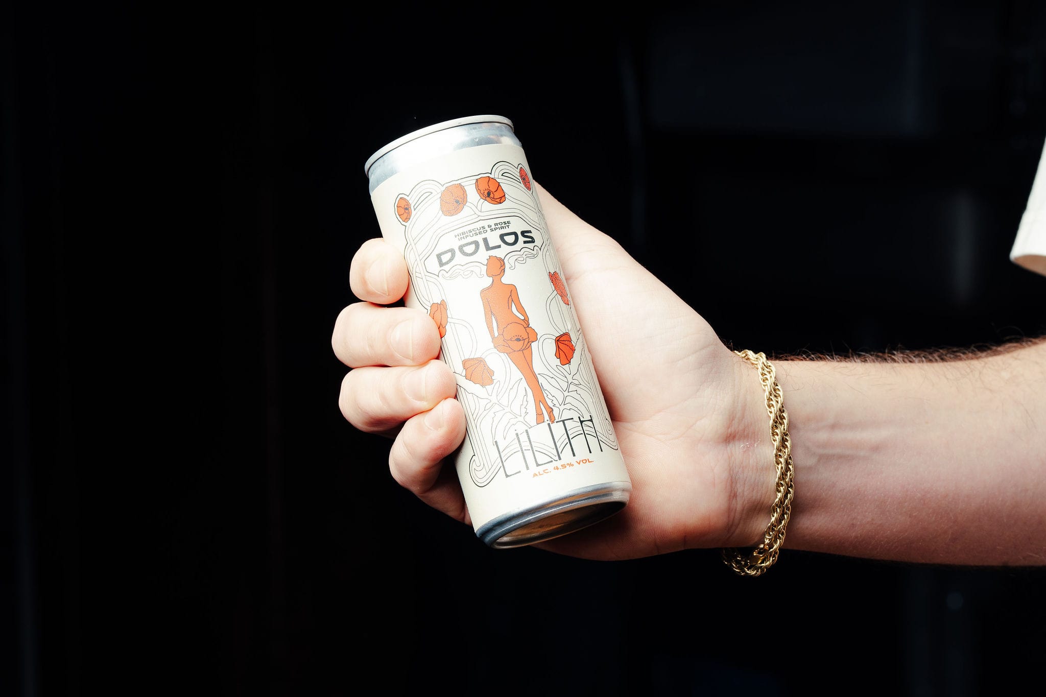 A hand with a gold bracelet holding a can of Dolos Lilith